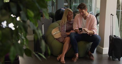 Happy Couple Relaxing at Hotel Lounge with Smartphone