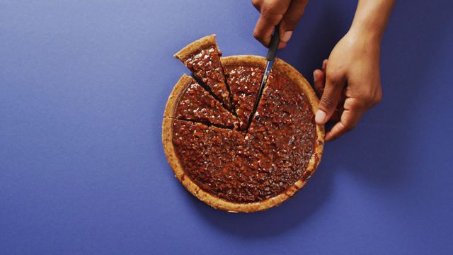 Highlighting a biracial man's hands cutting a delicious pecan pie on a blue background. Perfect for use in autumn celebration contexts, food blogs, dessert recipes, or holiday-themed promotions. Useful for illustrating traditional baking, festive events, or sweet dessert serving ideas.