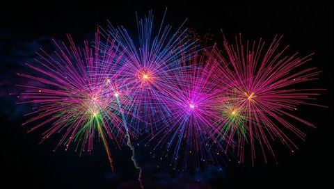 Vibrant fireworks bursting with vivid rainbow streaks and sparkling cores against dark sky