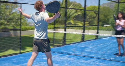 Male player swinging paddle on sunny blue padel court celebrating point win