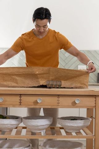 Asian man preparing indoor seedling tray with coir liner on wooden potting bench
