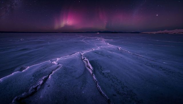 Cracked polar ice leading to purple aurora over starry horizon with violet fissures