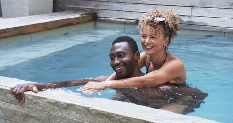 Couple enjoying plunge pool embrace on sunny deck, playful romantic summer retreat