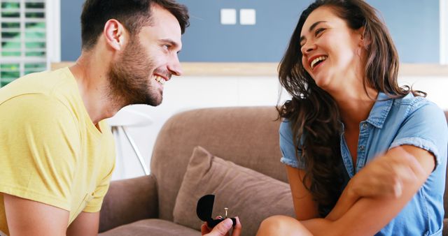 Man proposing to a happy woman at home. Perfect for engagement announcements, romantic story blogging, relationship advice articles, and advertising jewelry or wedding services.