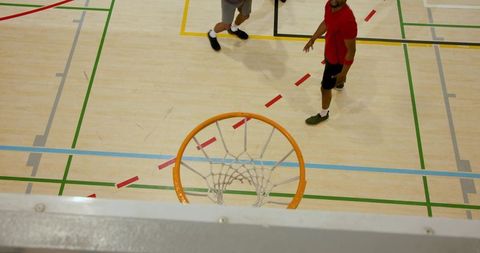 Aerial view showing basketball hoop and players moving on colorful indoor hardwood court