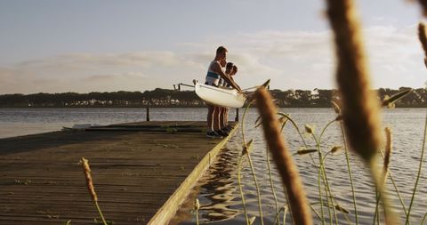 Team rowers preparing boat at sunlit lakeside dock