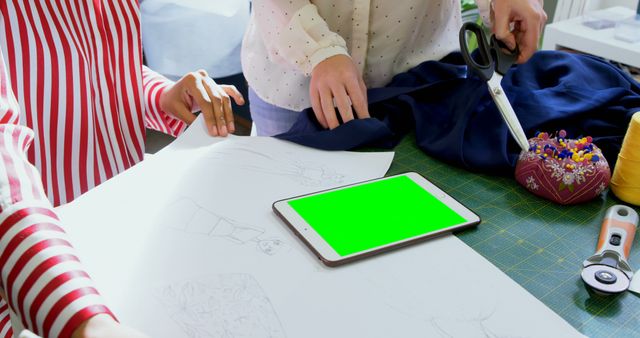 Two people collaborate on a sewing project, surrounded by tools and a tablet for guidance. - Download Free Stock Photos Pikwizard.com