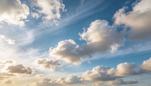 Golden sunlit cumulus clouds floating over wide blue sky with wispy cirrus streaks, serene panorama