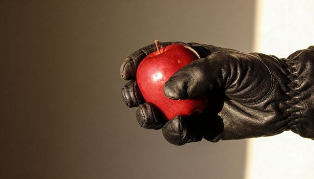Gloved hand offering shiny red apple against dramatic two-tone background, high contrast
