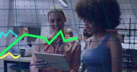 Reviewing tablet with interactive data graphs by female colleagues in open-plan office