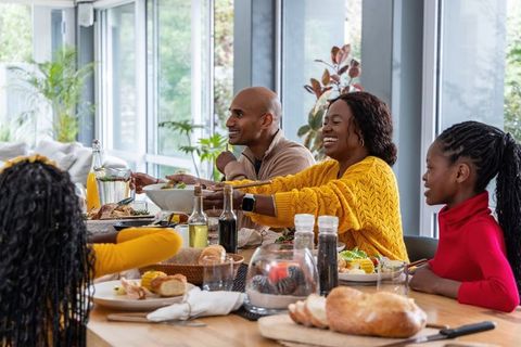 African american family sharing joyful brunch and serving bread at sunlit dining table