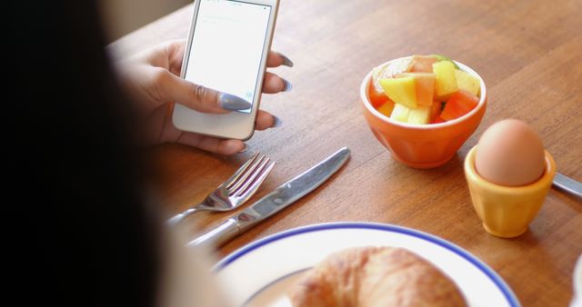 Woman using mobile phone while having breakfast at home