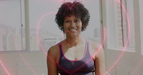 Smiling athletic woman wearing tank top in bright studio with neon heart overlays