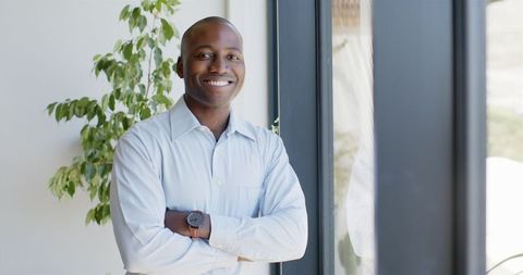 Confident Businessman Standing by Office Window Smiling Brightly