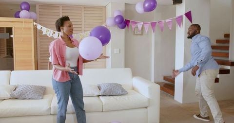 African American Couple Playing with Purple Balloons in Living Room Celebrating Home Party