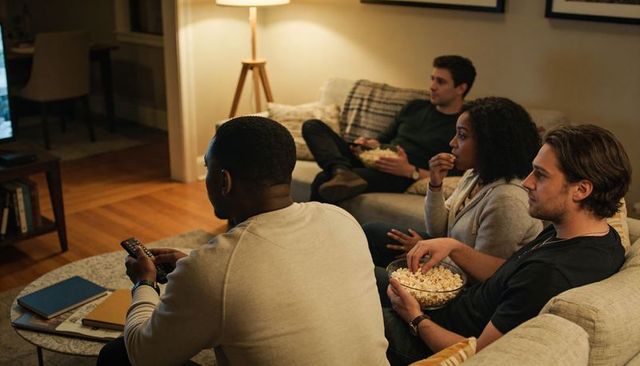 Friends watching movie night on cozy living room sofa sharing popcorn and remote control