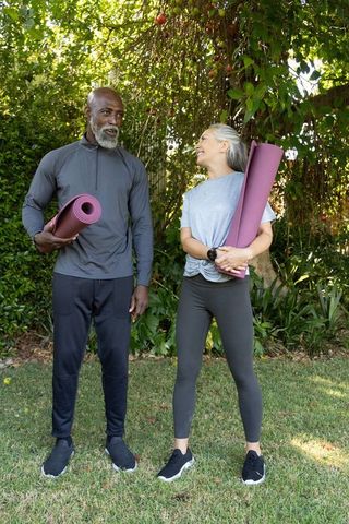 Mature couple standing with yoga mats in sunlit backyard practicing outdoor fitness and wellness