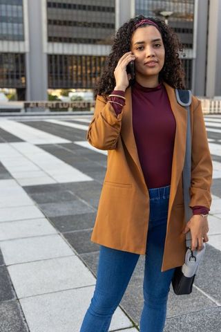 African american professional woman talking on phone in urban plaza wearing rust blazer