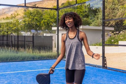 Laughing woman playing padel on blue court holding paddle wearing athletic clothing