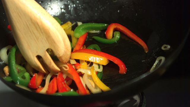 This video depicts a wooden fork mixing red, yellow, and green bell peppers along with onion slices in a heated wok. Ideal for cooking blogs, healthy eating websites, vegan recipes, and kitchen product advertisements. It emphasizes vibrant colors and dynamic motion suitable for promoting fresh, nutritious meal preparations.