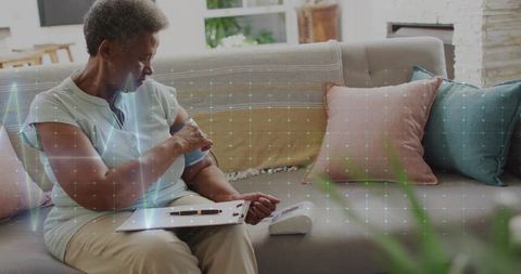 Senior woman monitoring blood pressure at home on couch with digital wrist cuff