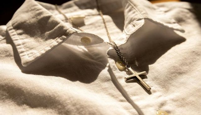 Gold cross pendant resting on white collared shirt closeup showing buttons and texture
