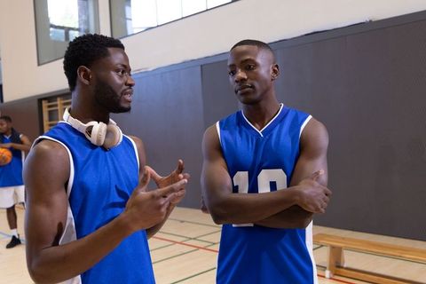 African american basketball players discussing strategy on gym court wearing blue jerseys