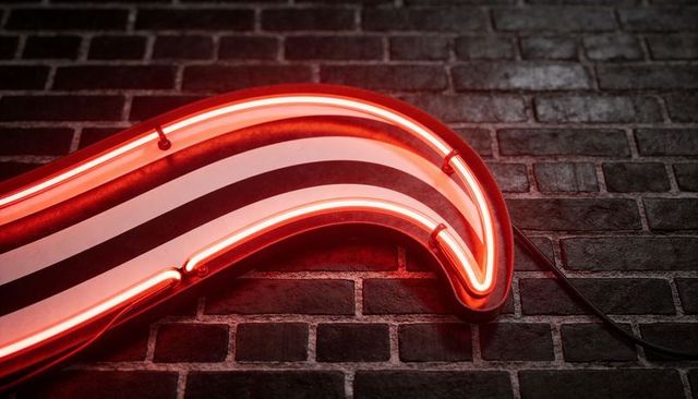 Curved red neon sign with white stripes casting warm glow on dark brick wall