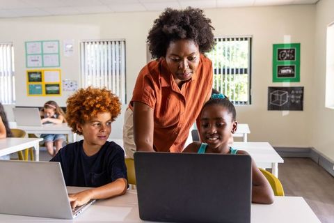 Teacher guiding students on laptops in classroom embracing digital learning and edtech