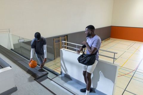 Basketball players preparing on indoor court mezzanine adjusting gym bag and dribbling