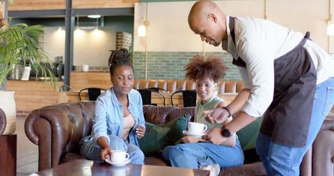 African American Friends Enjoying Coffee on Leather Sofa in Cozy Rustic Cafe