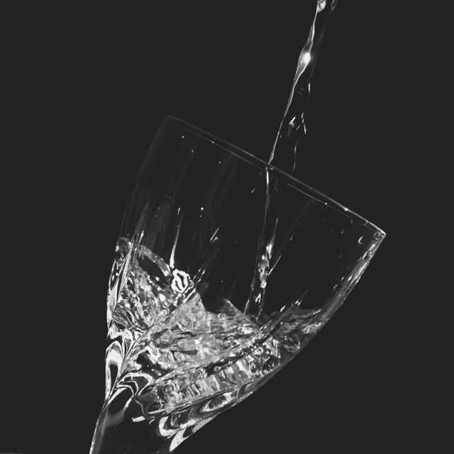 Close-up view of water being poured into a crystal glass, contrasting against a black background. This can be used for themes of purity, hydration, and refreshment, suitable for advertisements, health-related content, or beverage branding.