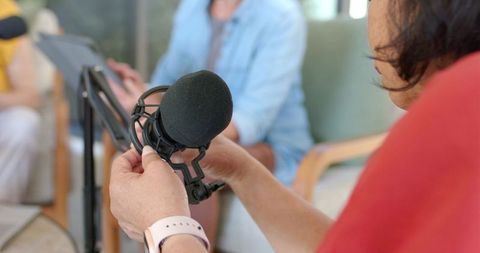 Asian senior adjusting foam-covered microphone on shock mount while recording podcast