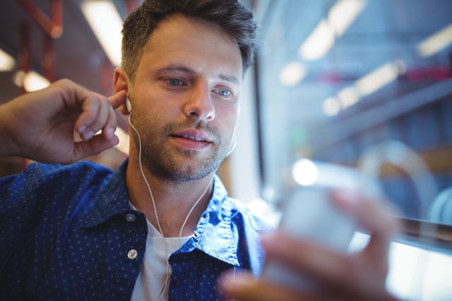 Young man enjoying music on his mobile phone while commuting by train. Ideal for use in articles or advertisements related to public transportation, technology, travel, urban lifestyle, and relaxation.