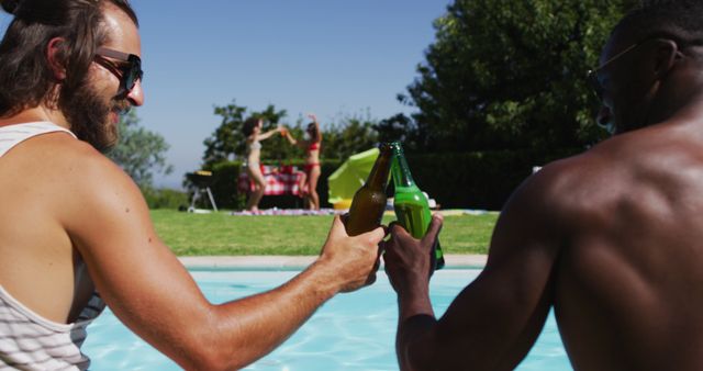 Two male diverse friends toasting and drinking beer while sitting by the pool. youth friendship and pool party concept