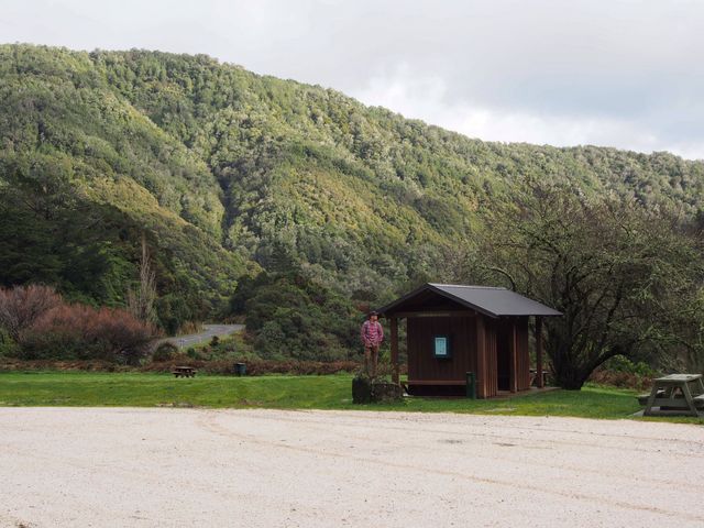 Wooden cabin located in picturesque valley with lush green forest hills in the background. Perfect for depicting serene and peaceful outdoors, engaging in hiking activities, promoting rural tourism, or use in nature-themed editorials.