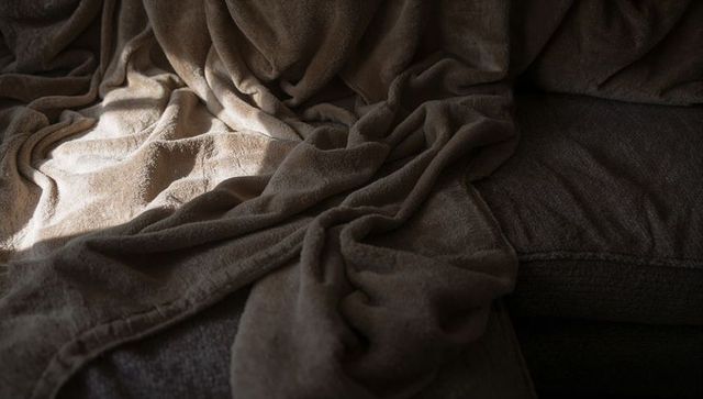 Draping brown fleece blanket catching warm sunlight on sofa seat showing plush texture