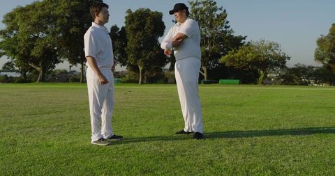 Young cricket teammates discussing tactics on sunlit outfield wearing white uniforms