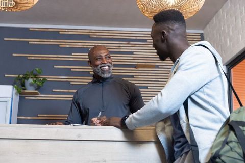 African american receptionist smiling while guest signing at modern wood-slat lobby desk