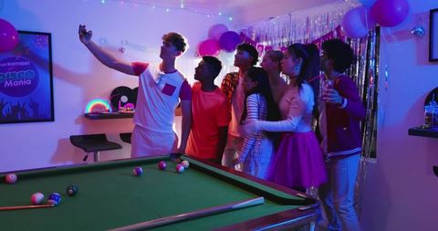 Diverse friends taking selfie at neon disco birthday party with pool table