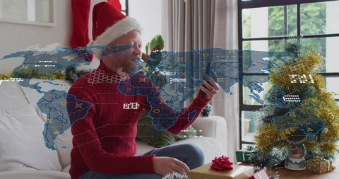 Senior man wearing santa hat video calling with holographic map near christmas tree and gifts
