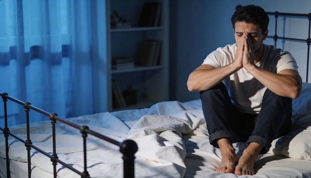 Man Sitting on Bed Holding Face in Hands Late Night Contemplating Stress and Insomnia