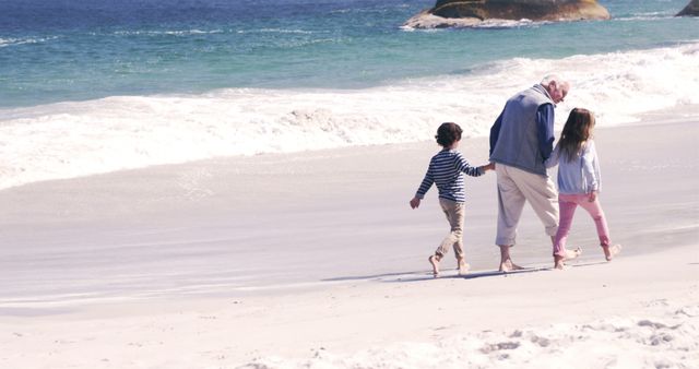 Grandfather walking with children on sandy beach near ocean with waves. Ideal for promoting family outings, multigenerational bonding, senior lifestyle, vacations, holiday destinations, and quality time concepts.