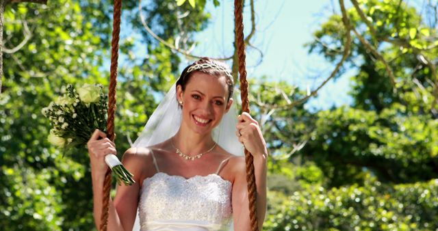 Happy bride sitting on a swing looking at camera on her wedding day