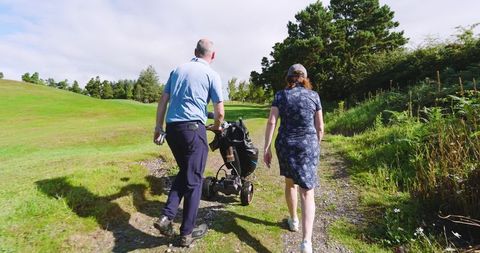 Golf partners walking with trolley on scenic fairway