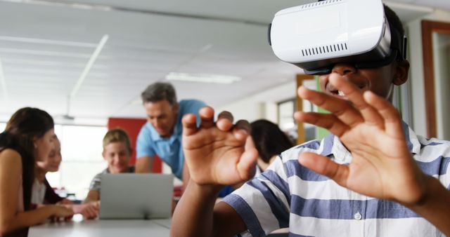 Students in a classroom are using virtual reality headsets for an interactive learning experience. Teachers and classmates collaborate in the background at a computer. This image can be used for educational and technology-related content, highlighting modern teaching methods and innovative classroom activities.