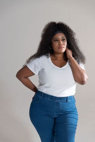 Standing confident african american woman wearing white ribbed top and high-waisted denim
