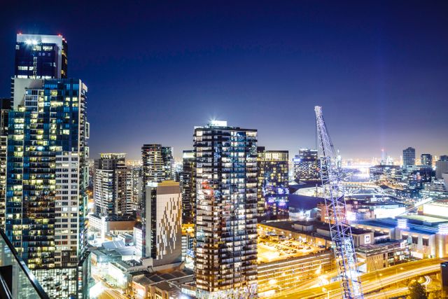 This vibrant cityscape captures a bustling urban environment at night with prominent illuminated skyscrapers and ongoing construction. Suitable for highlighting modern city life, urban development, architectural projects, and the dynamic energy of business districts. Perfect for promotional materials, real estate brochures, and city planning presentations.