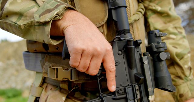 Soldier pointing at rifle trigger guard, emphasizing weapon safety or readiness for combat. Useful for articles, training materials, or publications about military tactics and weapon handling.