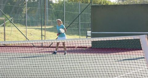 Female tennis player practicing on sunny outdoor court holding racket and preparing shot